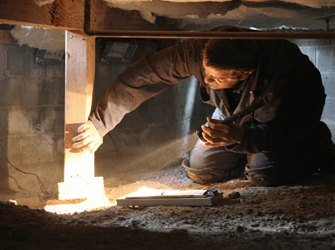 A professional inspecting wooden beams under the floor of a structure in Aurora, IL